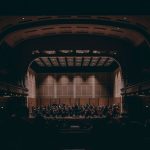 Orquestra sinfônica se apresenta no palco de um teatro histórico durante um concerto.