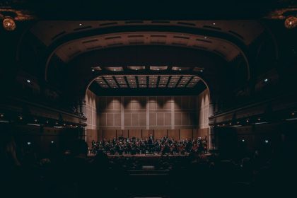 Orquestra sinfônica se apresenta no palco de um teatro histórico durante um concerto.