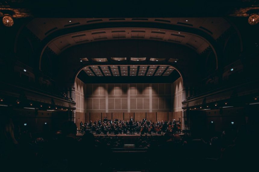 Orquestra sinfônica se apresenta no palco de um teatro histórico durante um concerto.