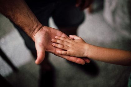 Mão de uma criança repousa sobre a mão de um adulto, simbolizando cuidado, apoio e proteção.