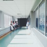 Corredor iluminado de hospital com profissionais de saúde usando jalecos brancos.