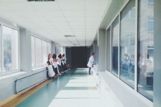 Corredor iluminado de hospital com profissionais de saúde usando jalecos brancos.