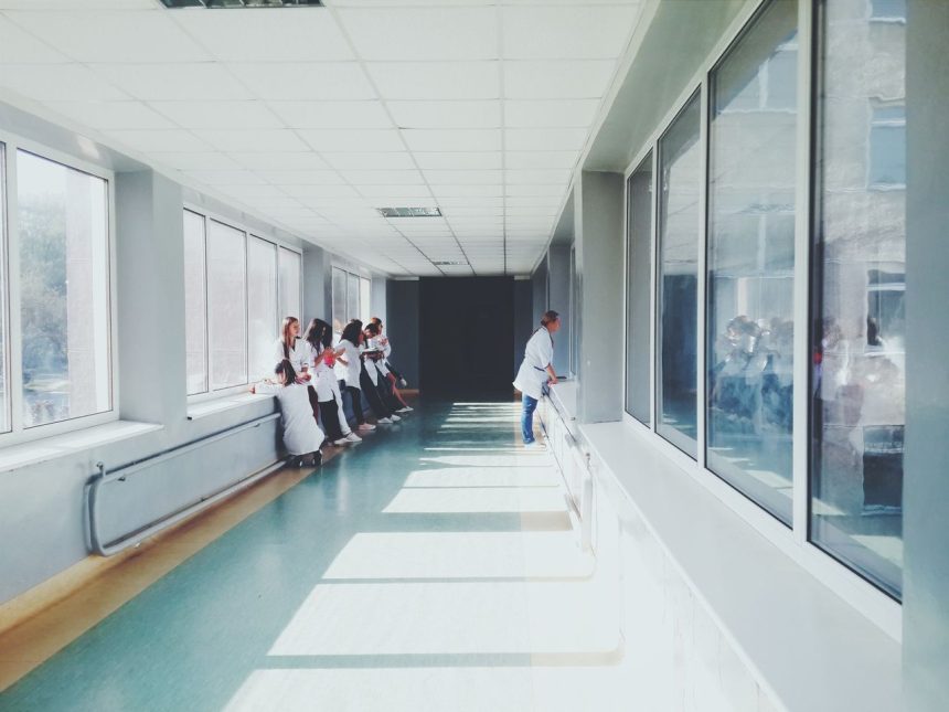 Corredor iluminado de hospital com profissionais de saúde usando jalecos brancos.